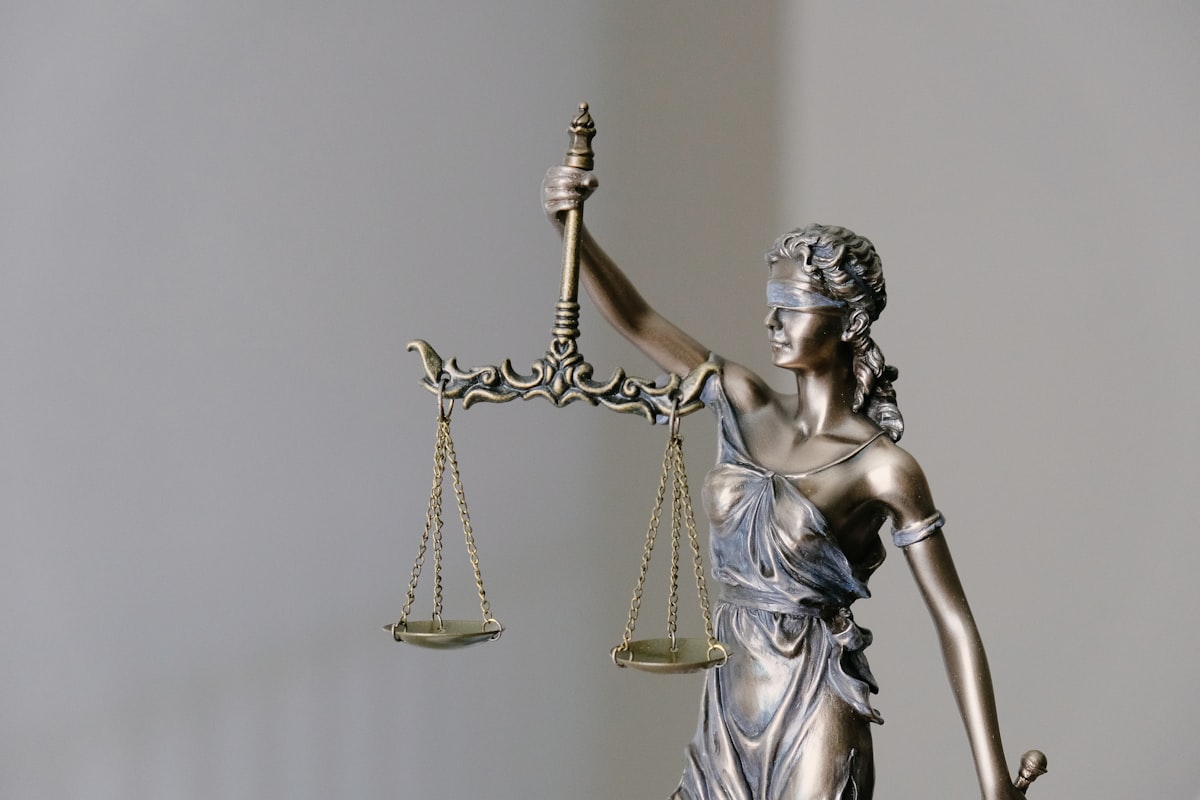 Estátua da Dama da Justiça em primeiro plano, prateleiras com livros jurídicos ao fundo