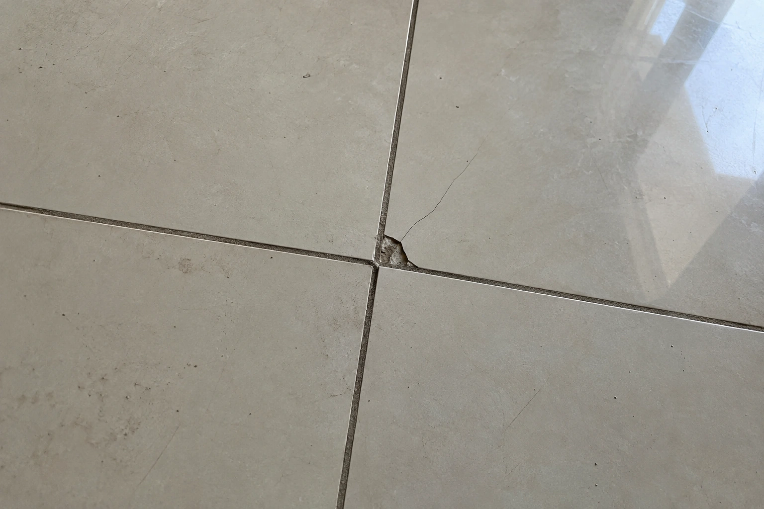 Detalhe de um piso claro com uma pequena quebra e marcas na junta, registrado de perto durante a vistoria